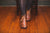 Women's Brown Handmade North Pacific Boots on model with black tights sitting in chair on wood floor.