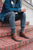 Man sitting on brick steps, wearing jean jacket, rolled pants, grey socks, and brown North Pacific handmade leather boots by Aurora Shoe Co.